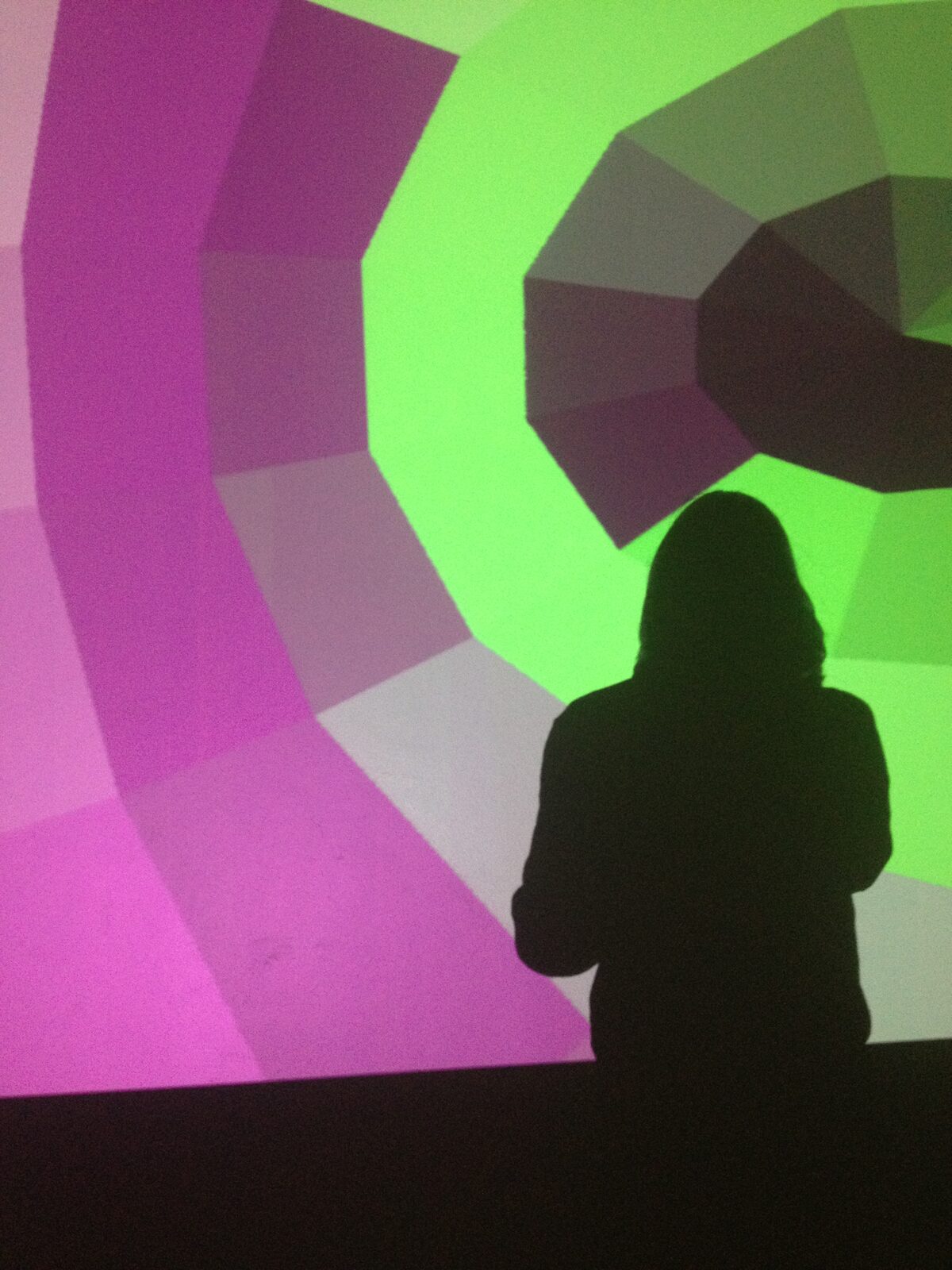 A person silhouetted inside a large magenta and green faceted projection on a wall